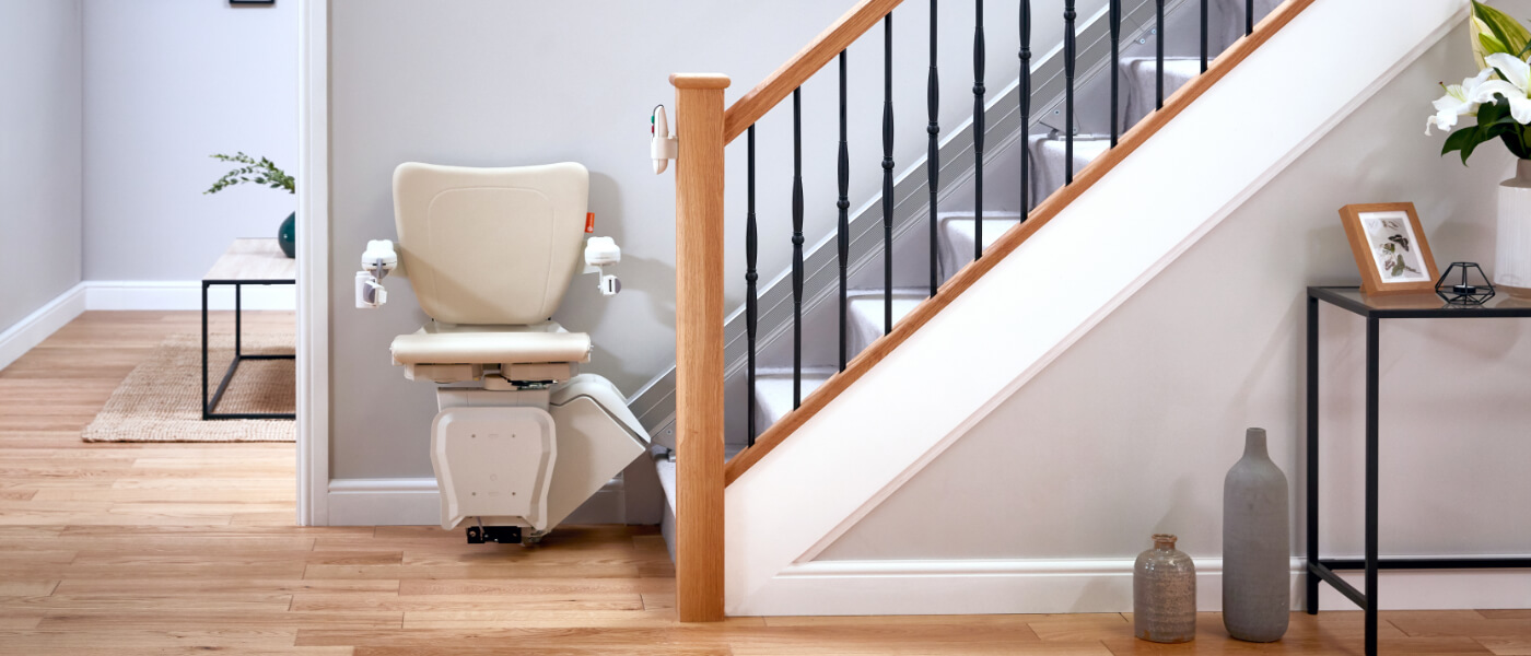 Straight stairlift in cream colour at the bottom of a flight of stairs