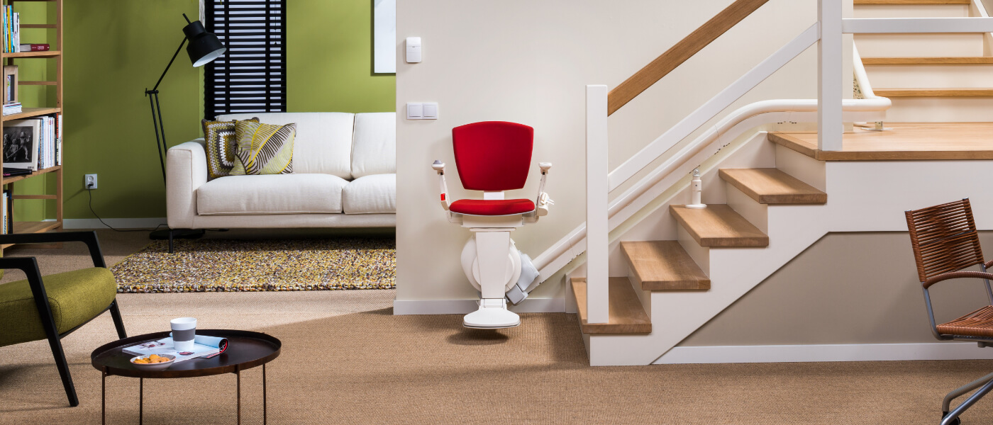 Curved stairlift in with with red cushion at bottom of wooden curved staircase